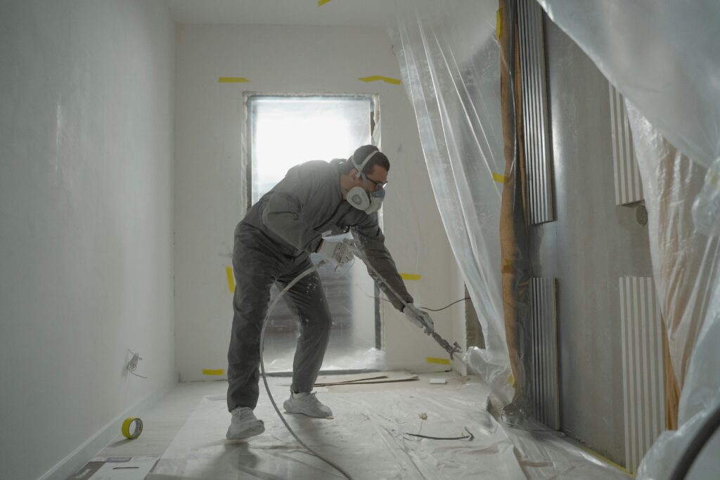 A worker in protective gear painting walls during an indoor renovation project.